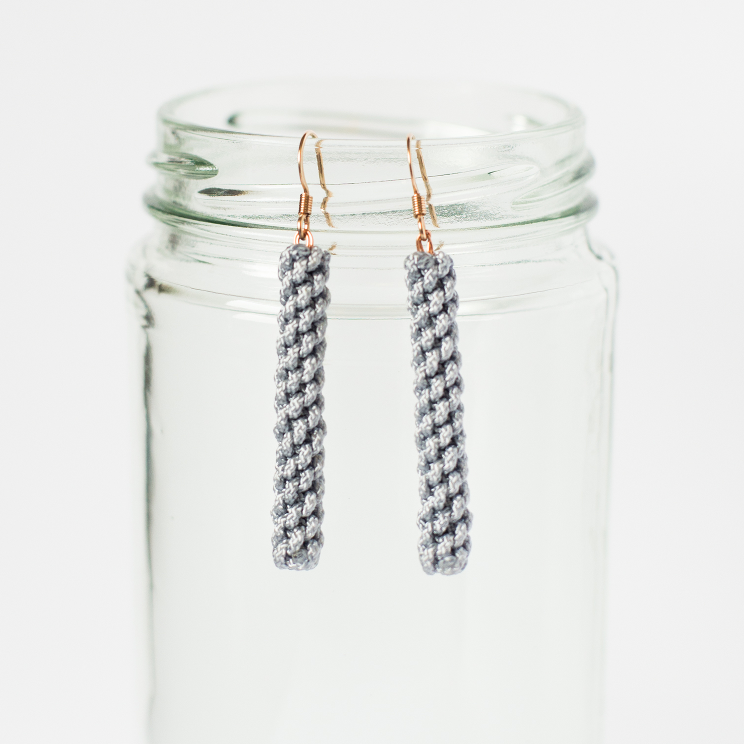 Gray woven dangle earrings with gold hooks displayed on a clear glass jar