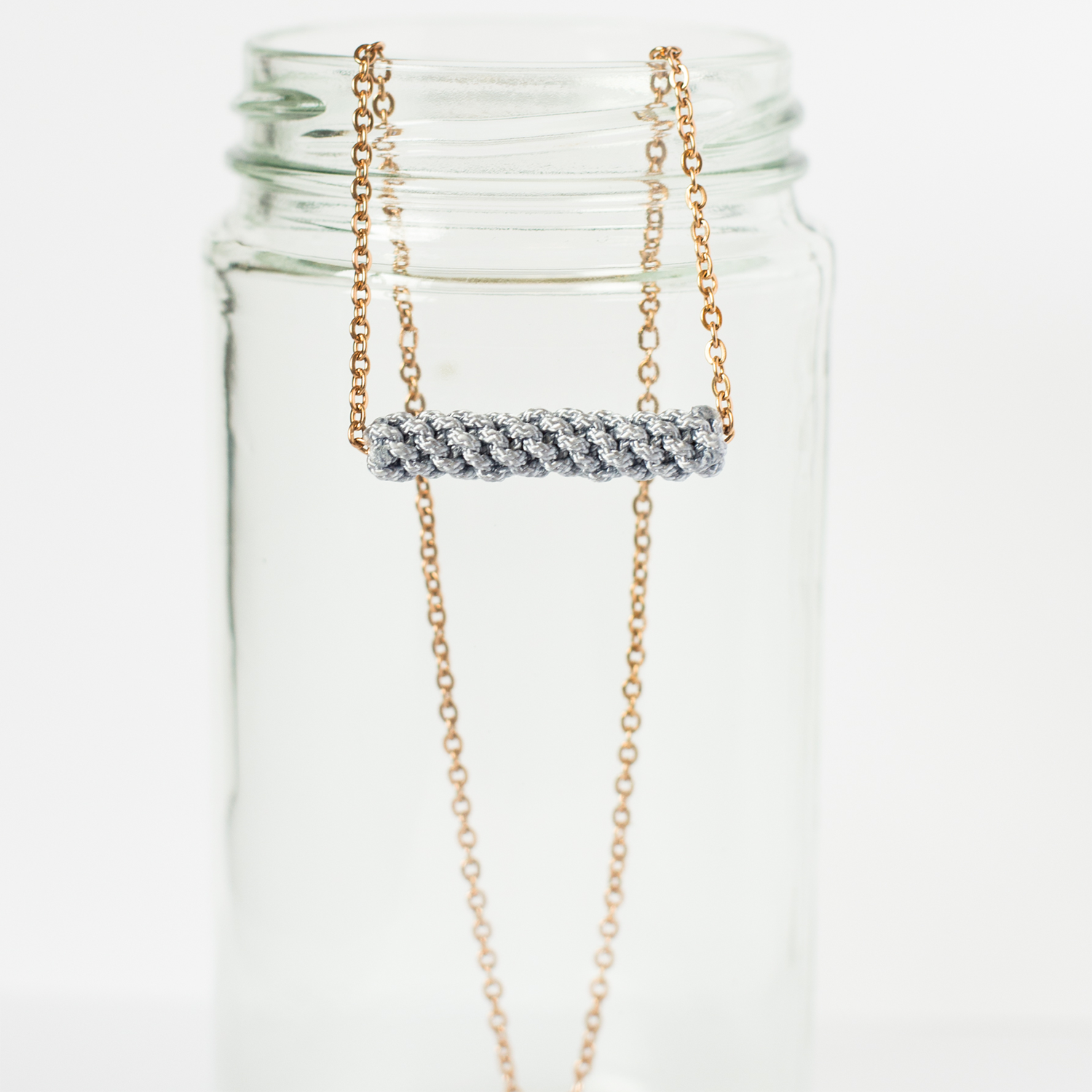 Minimalist silver and gold chain necklace with twisted cord pendant displayed on a clear glass jar